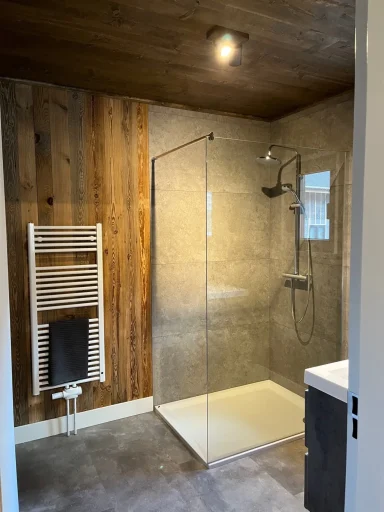 Moderne badkamer met glazen douche, houten wand en verwarmde handdoekradiator.